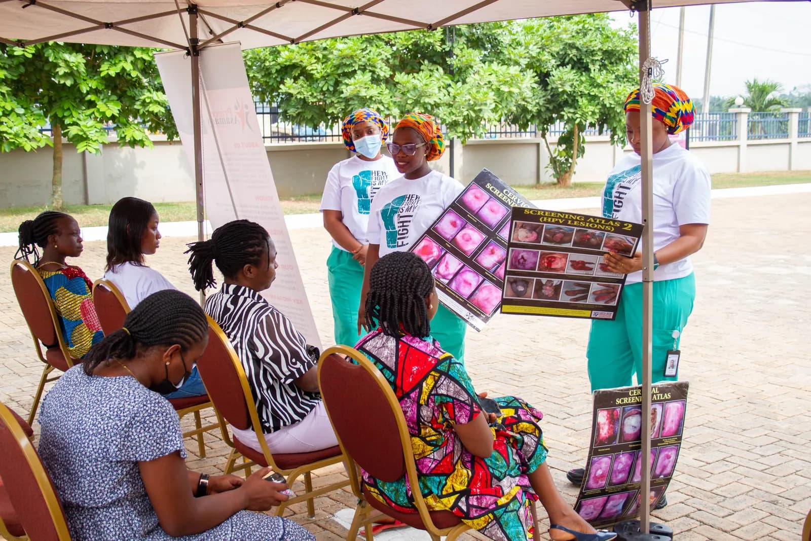 Health educator presenting a cervical cancer health guide to seated women at a community screening outreach